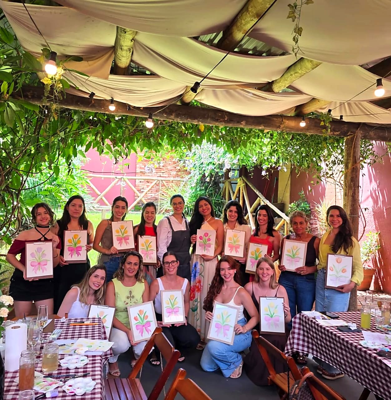 Grupo de mulheres em oficina de aquarela ao ar livre, mostrando suas pinturas de flores